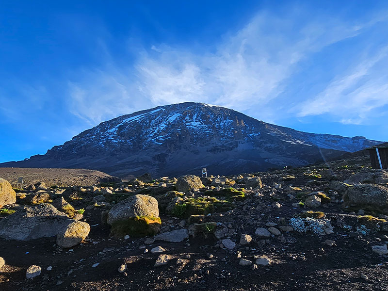 Sweeping view of Mount Kilimanjaro’s Kibo Peak from Karanga Camp on the Shira Route, with rocky alpine terrain under a bright morning sky | Kili Quests