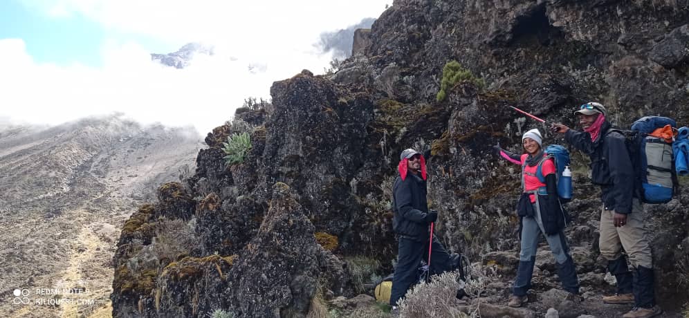 Trekkers climbing the rocky Barranco Wall on Kilimanjaro’s Umbwe Route, with misty skies and steep volcanic terrain in the background | Kili Quests