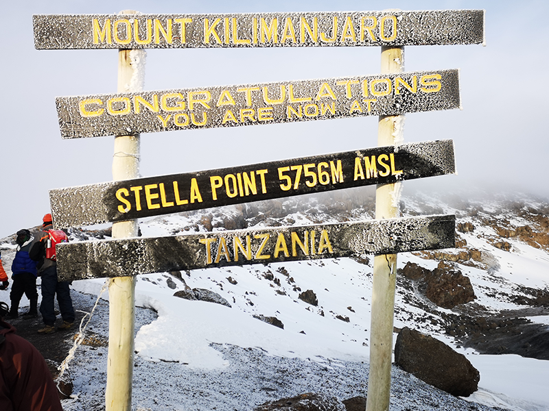 Stella Point signpost on Mount Kilimanjaro’s crater rim, frosted with snow and showing an elevation of 5,756 meters above sea level.