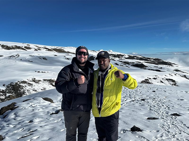 Kilimanjaro guide and climber standing together at Stella Point, sharing a moment in fresh snow