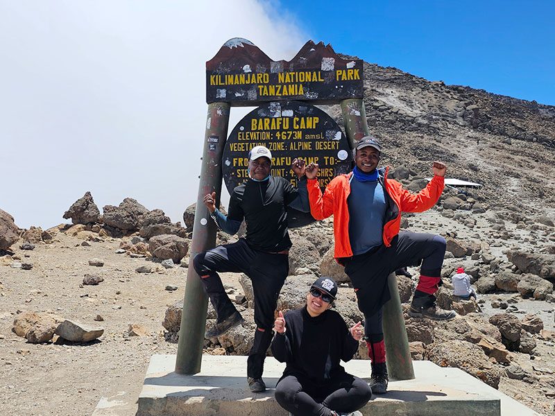 Smiling climbers posing at Barafu Camp (4,673m) on the Umbwe Route, striking fun poses before starting their summit ascent to Uhuru Peak | Kili Quests
