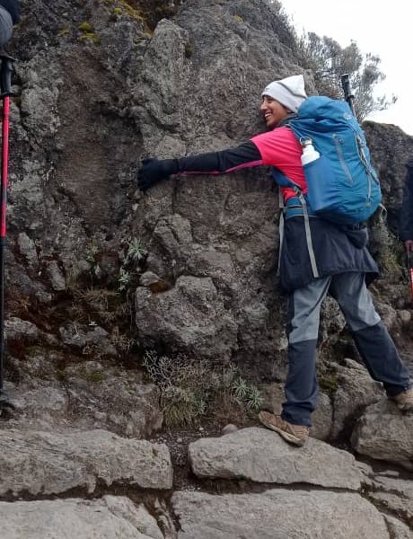 Trekker climbing and hugging a rock on Kilimanjaro’s Barranco Wall, a fun and scenic segment encountered on the Northern Circuit via Lemosho | Kili Quests
