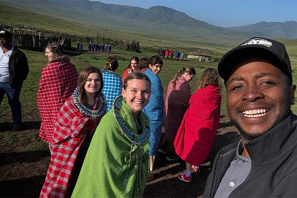 : Tourists visiting a Maasai boma in Tanzania, engaging with Maasai elders and families