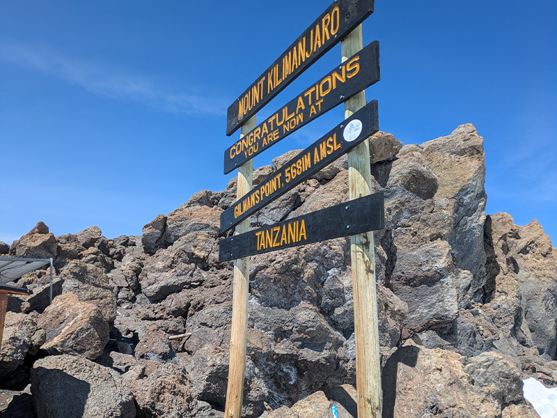 Gilman’s Point summit sign on Mount Kilimanjaro, located at 5,681 meters above sea level, with rocky terrain and clear blue sky.