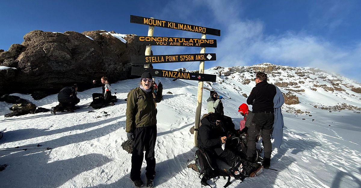 Trekkers and porters standing together at Stella Point sign on Mount Kilimanjaro