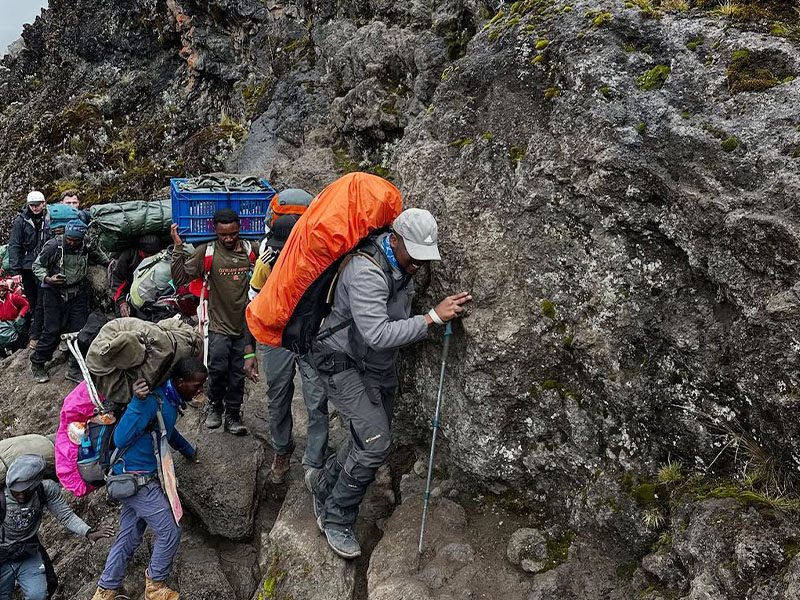Trekkers and porters carefully ascending the Kissing Rock section on Barranco Wall along the Machame Route, Kilimanjaro | Kili Quests