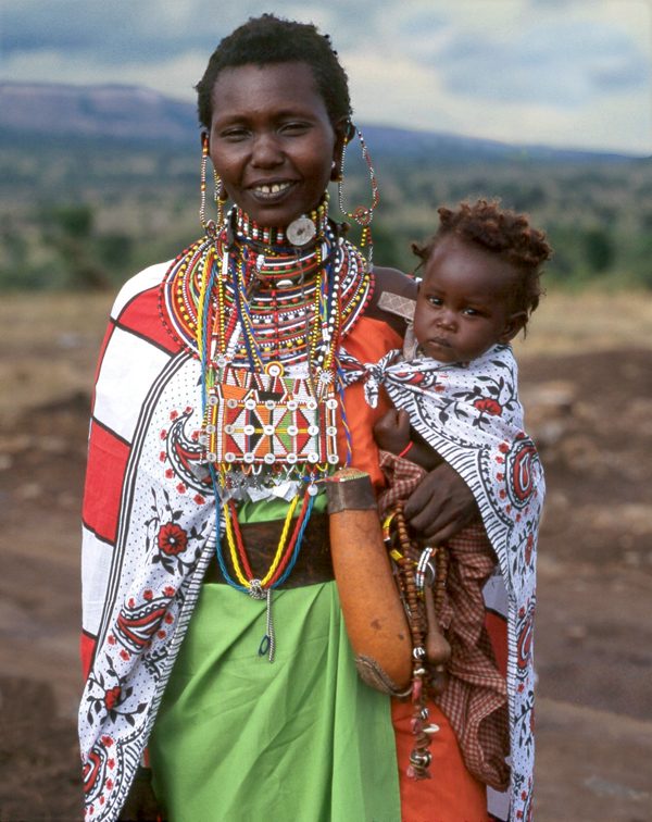 Maasai woman in traditional dress carrying a child on her back, wrapped in colorful fabric