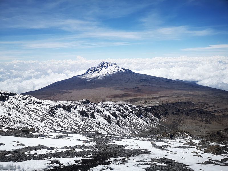 View of Mawenzi Peak from Stella Point on Mount Kilimanjaro, with snow-covered terrain and clouds below — typical scenery on the Rongai Route | Kili Quests