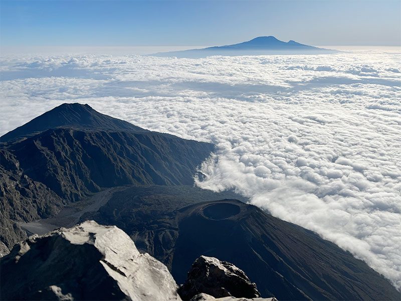 : Mount Meru and Mount Kilimanjaro seen from a distance across the Tanzanian plains