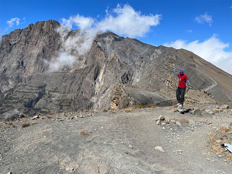 Trekker approaching the final ridge to Socialist Peak, the summit of Mount Meru, with steep volcanic cliffs in the background | Kili Quests