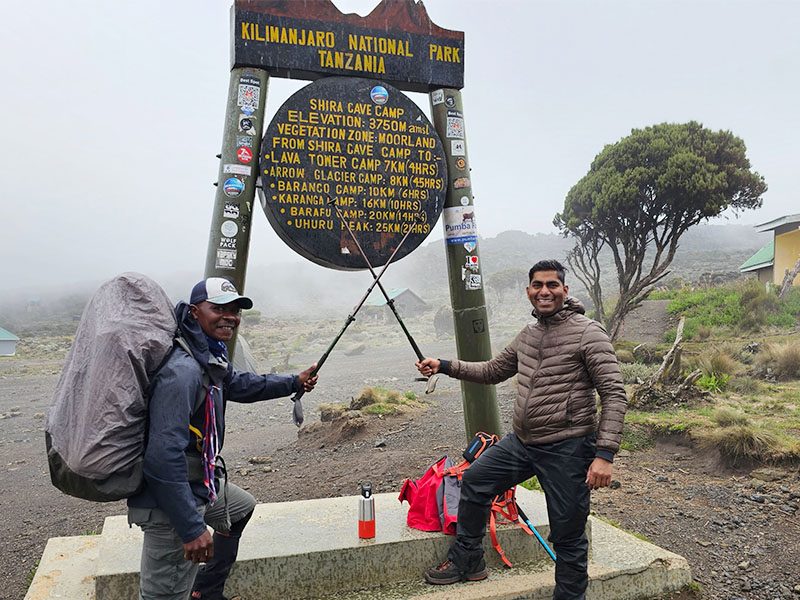 Trekkers posing with hiking poles at the Shira Cave Camp sign on Day 2 of the Machame Route, Kilimanjaro | Kili Quests