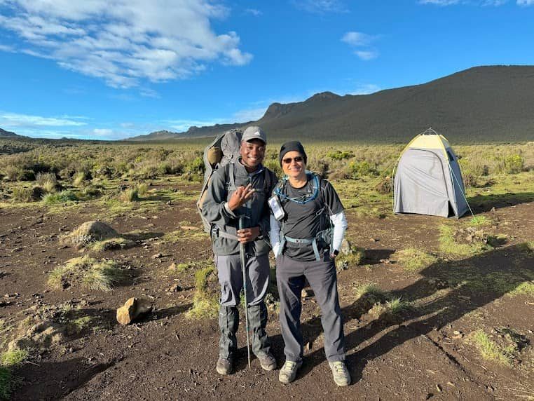 Two trekkers standing at Shira One Camp on the Lemosho Route, Kilimanjaro, with scenic moorland and tent in the background | Kili Quests