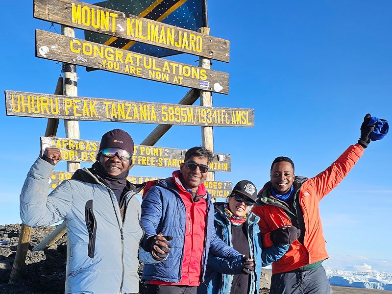 Climber standing at Uhuru Peak sign on the summit of Mount Kilimanjaro